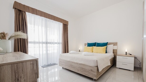 Une chambre d’hôtel moderne avec un grand lit, une table de chevet, un bureau et une fenêtre avec des rideaux.