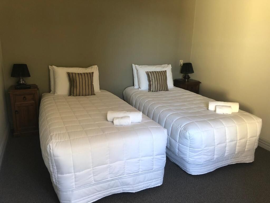 Two single beds with white bedding and striped pillows, each with a small table and a lamp beside it.