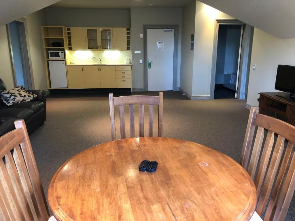 Ein Wohnzimmer mit einem Holzespeisetisch, einer schwarzen Couch und einer Küche im Hintergrund.