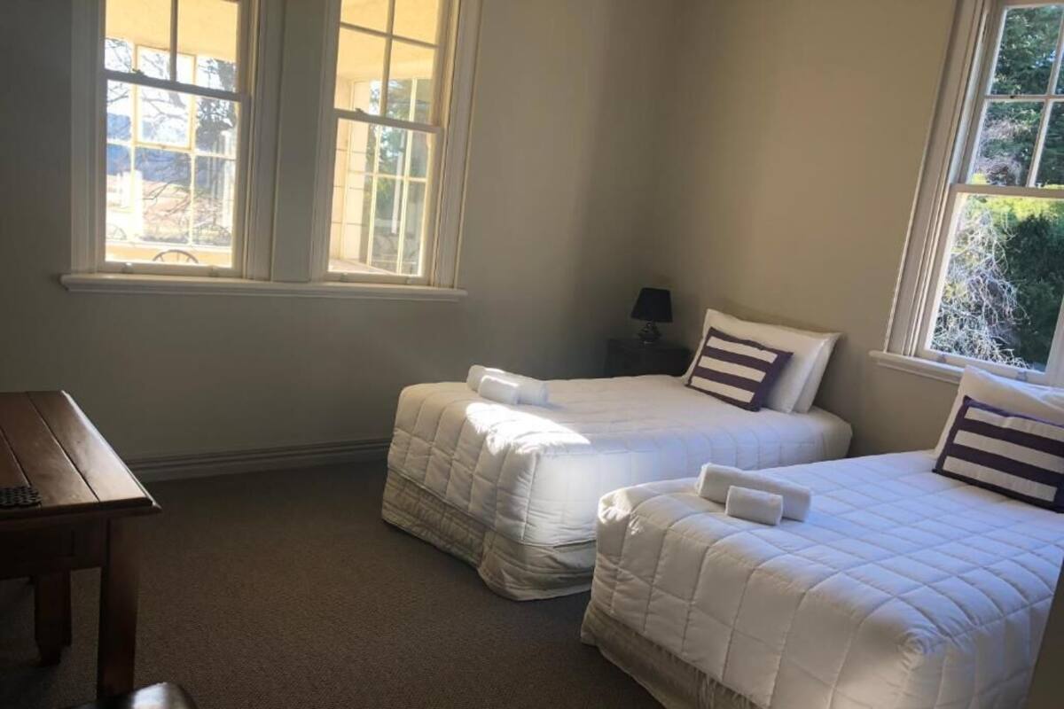 A bedroom with two beds, a small table, and a window with a view of trees.