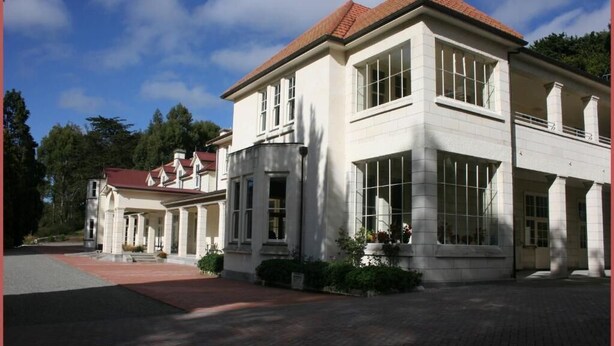 A two-story building with a symmetrical facade, large windows, and a red-tiled roof.