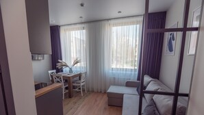 A modern living room with a wooden floor, a sofa, a dining table with chairs, and a kitchen area with a stove. - Contactless check-in, functional area of ​​the apartment, workplace (Lviv)
