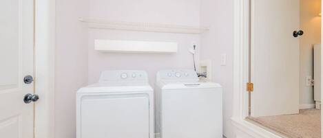 A laundry room with two white front-loading washing machines and a white shelf above them.