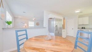 Una cocina moderna con armarios blancos, un refrigerador de acero inoxidable y una mesa de comedor redonda de madera con sillas azules.