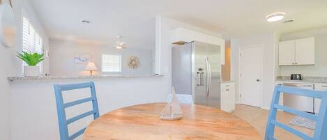 Una cocina moderna con armarios blancos, un refrigerador de acero inoxidable y una mesa de comedor redonda de madera con sillas azules.