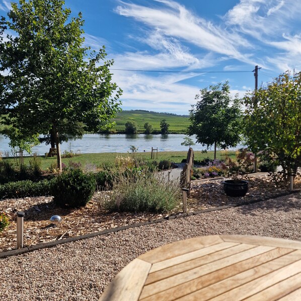A lakeside view with a wooden deck, a stone pathway, and a view of the lake and hills.