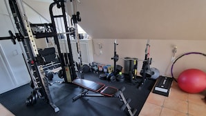 Une salle de sport à domicile équipée d'un support à squats, d'un banc de développé couché, d'haltères, de kettlebells et d'un ballon lesté.