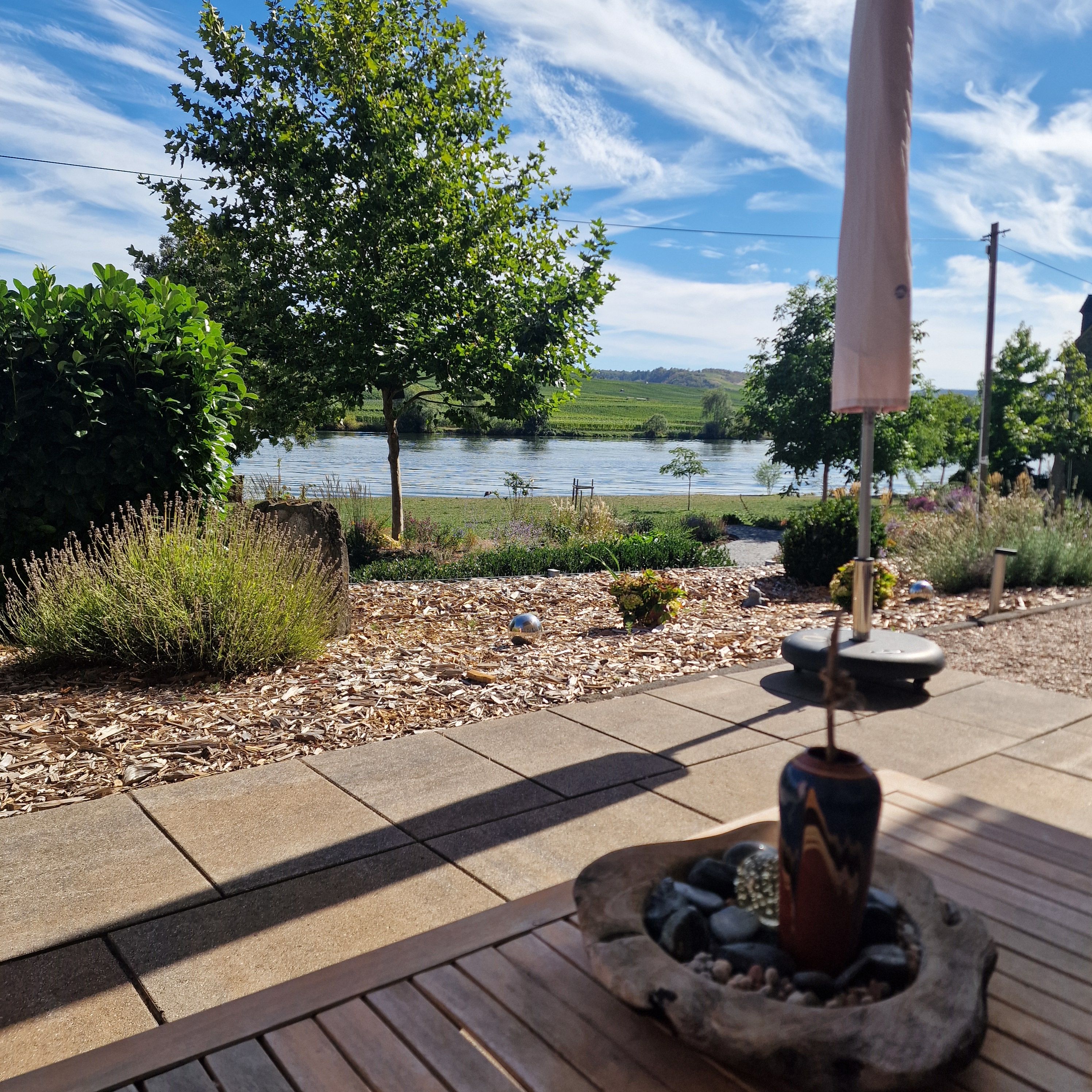 Un espace patio offrant une vue sur un lac, entouré de verdure et agrémenté d’un chemin en pierre.