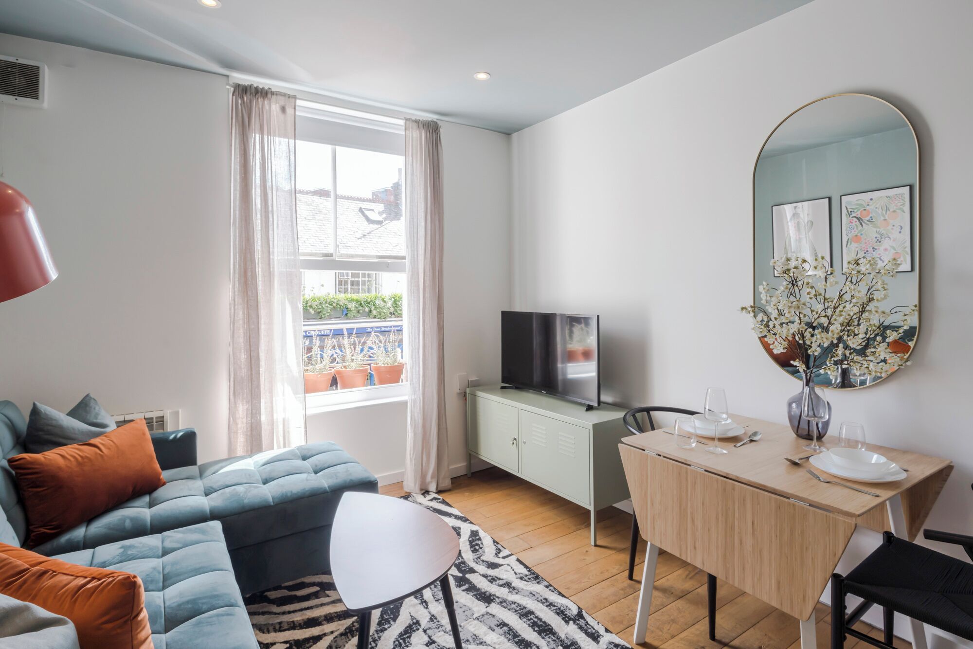 A modern living room with a sofa, a dining table, a TV, and a view of the outside.