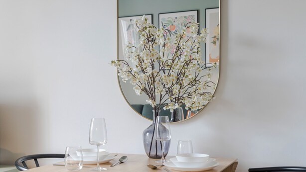A dining table with a vase of white flowers, clear wine glasses, and white plates.