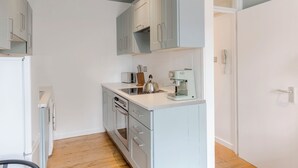 A compact kitchen with white cabinets, a built-in oven, and a coffee machine.