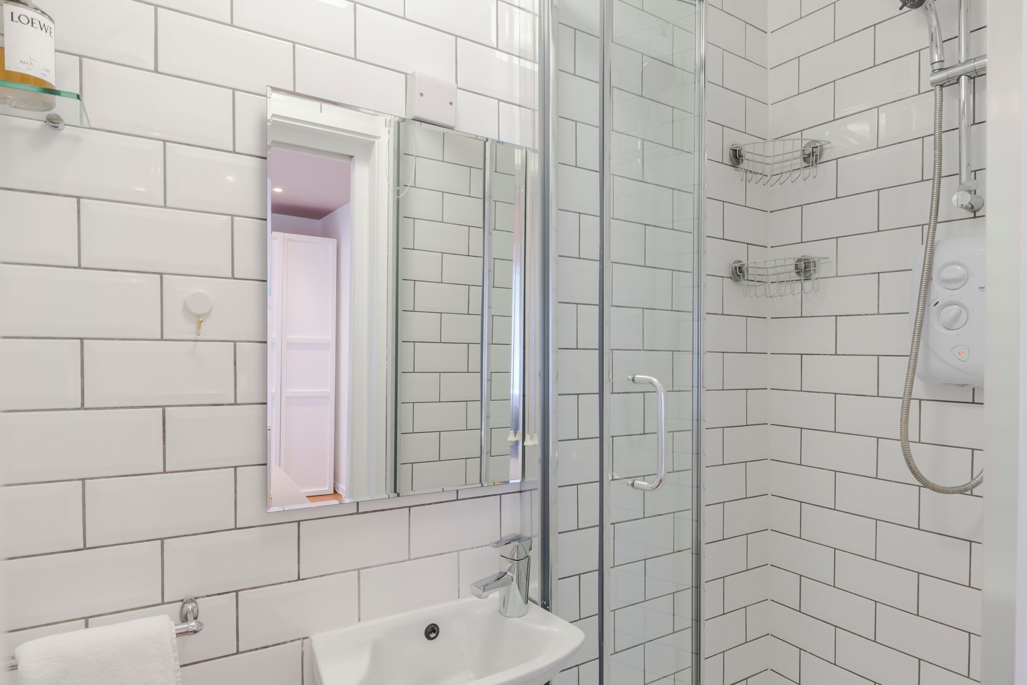 Une salle de bain moderne avec des carreaux de céramique blancs rectangulaires, une douche en verre, un lavabo avec un miroir et des toilettes.