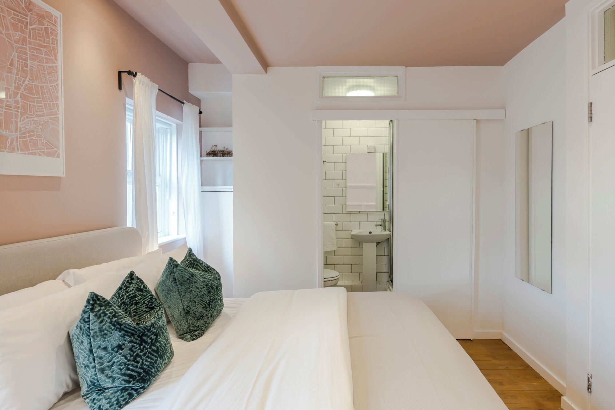 A bedroom with a large bed, a window with curtains, a map on the wall, and a bathroom visible through an open door.