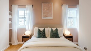 A bedroom with a bed, two bedside tables with lamps, a map on the wall, and a window with curtains.