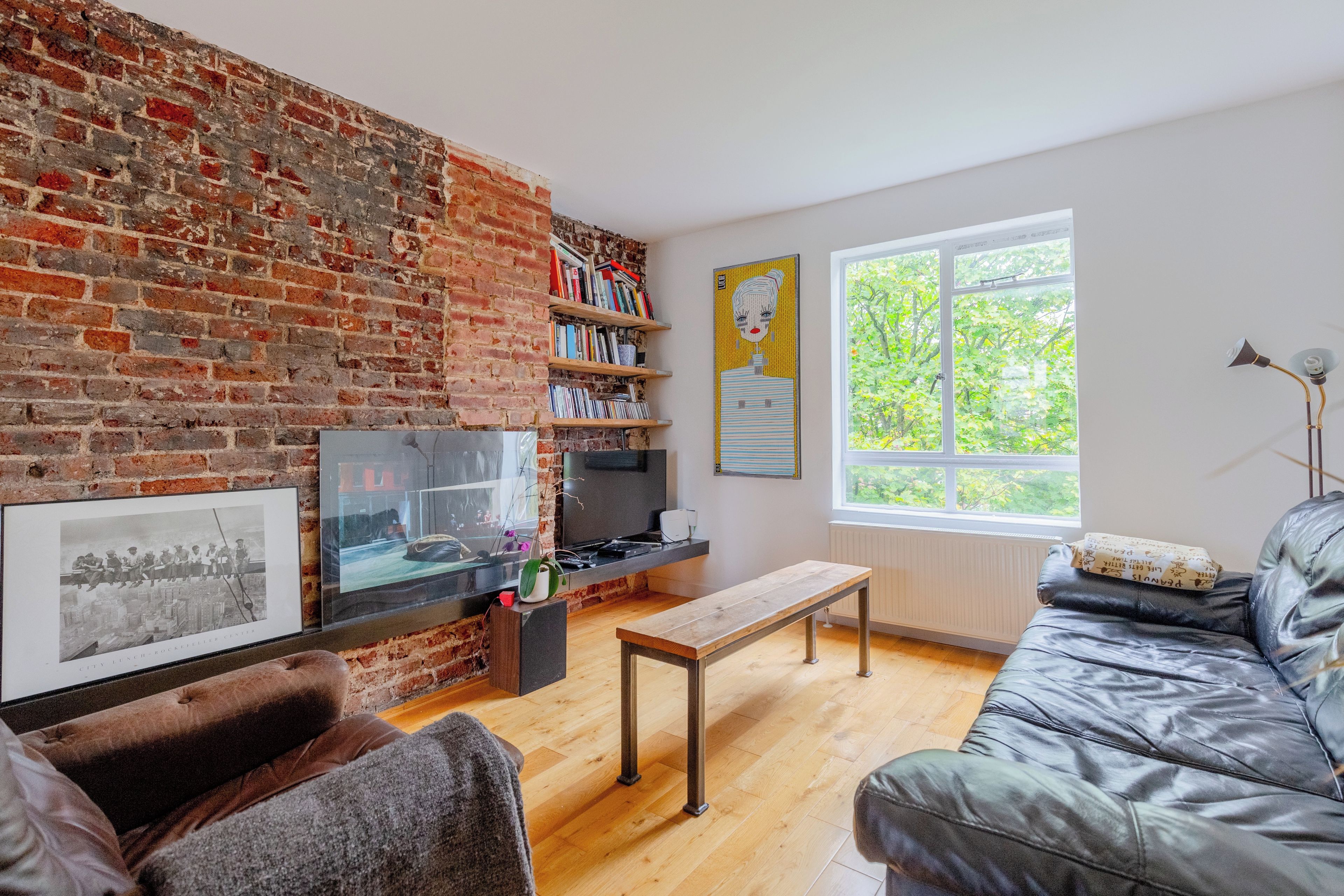 Ein Wohnzimmer mit Backsteinwand, Bücherregal, Flachbildfernseher, einer Bank und einem Ledersofa.