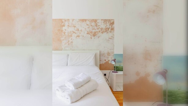 Une chambre à coucher avec un lit, des oreillers, une serviette soigneusement pliée, une table de chevet, une lampe et un tableau accroché au mur.