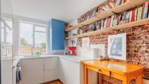 Une cuisine avec des meubles blancs, une table en bois, un mur en briques et une fenêtre.