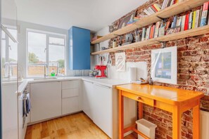 A kitchen with white cabinets, a wooden table, a brick wall, and a window. - 1BD Loft Style Flat in the Heart of Islington (Greater London)
