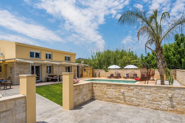 Una casa moderna con piscina, mobiliario de exterior y un muro de piedra.