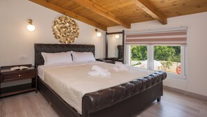 Ein Schlafzimmer mit einem großen Bett, Holzbalkendecke, Nachttisch und einem Fenster mit Blick auf Grünflächen.
