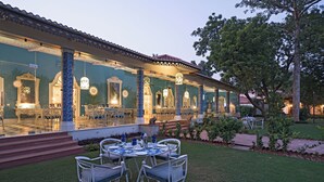 An outdoor dining area with a covered patio, a pool, and a well-maintained lawn. - Raj Niwas Palace (Dhaulpur)