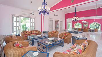 A spacious living room with wicker furniture, a chandelier, and large windows.