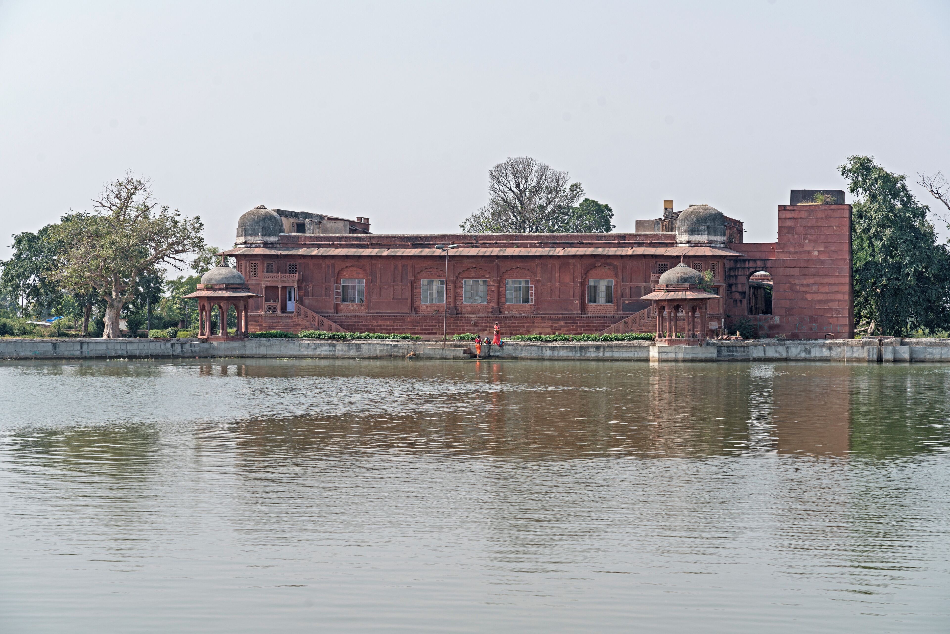 A large, historic building with domed structures and a reflective water body in front.
