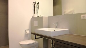 Un baño moderno con inodoro blanco, un lavabo rectangular y un espejo sobre él.