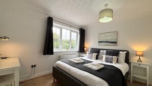 Une chambre à coucher avec un grand lit, une fenêtre avec des rideaux, une table de chevet avec une lampe et un luminaire au plafond.