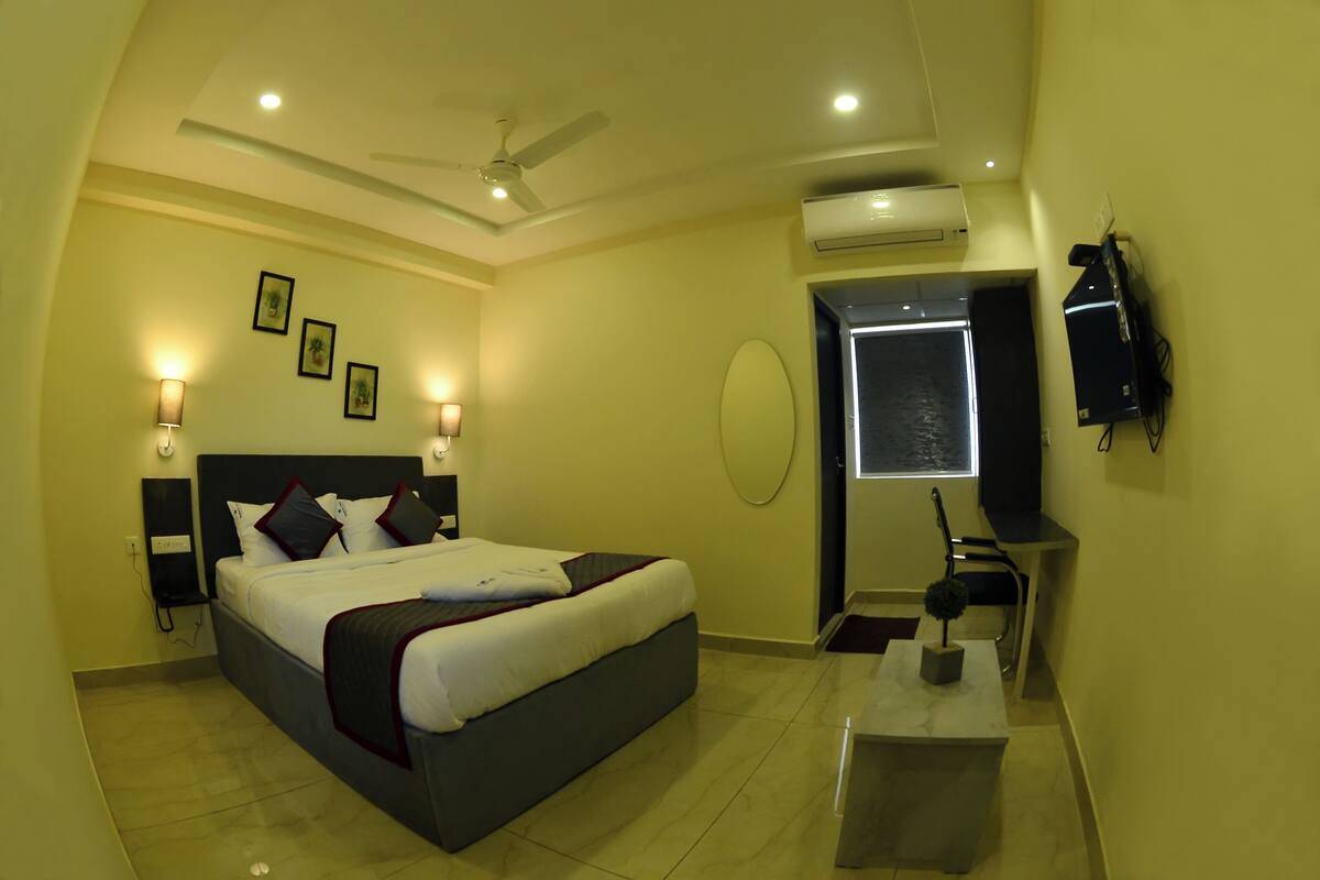 A hotel room with a bed, bedside lamps, an air conditioning unit, a ceiling fan, a TV, and a small table with a decorative item.