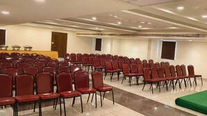 A conference room with rows of red chairs, a stage with a yellow backdrop, and a buffet table. - Seasons Stay (Vijayawada)
