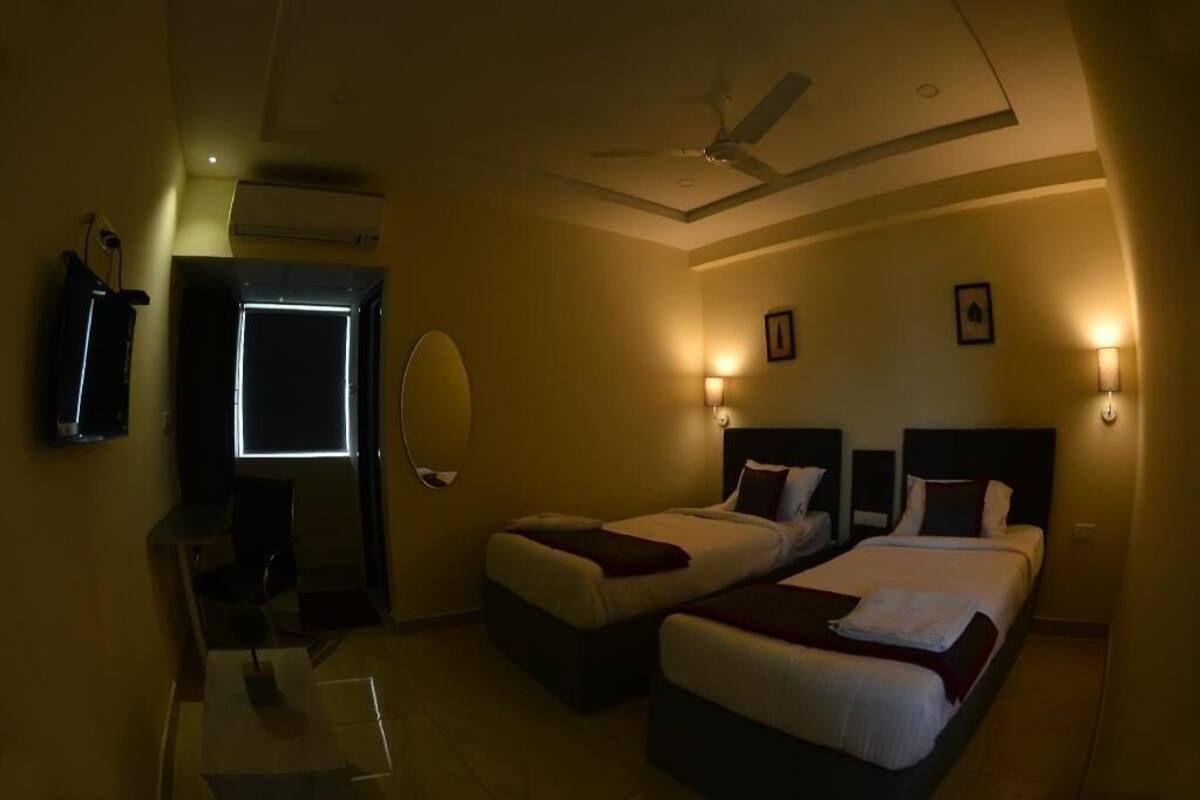 A hotel room with two beds, a ceiling fan, wall-mounted lights, a TV, and a mirror.