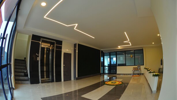 A modern lobby with a marble floor, a staircase, and a reception area with a flower arrangement. - Seasons Stay (Vijayawada)