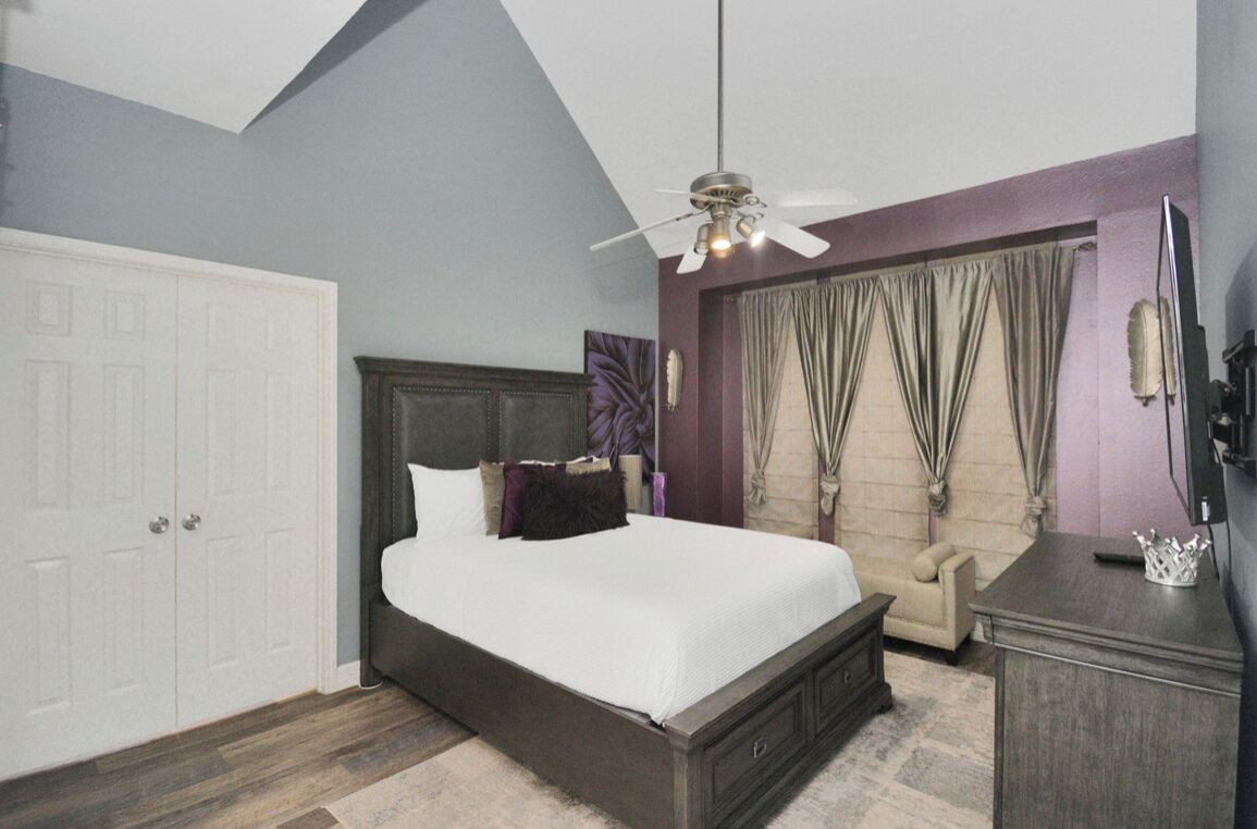 Une chambre à coucher avec un lit, un ventilateur de plafond, une commode et un téléviseur.