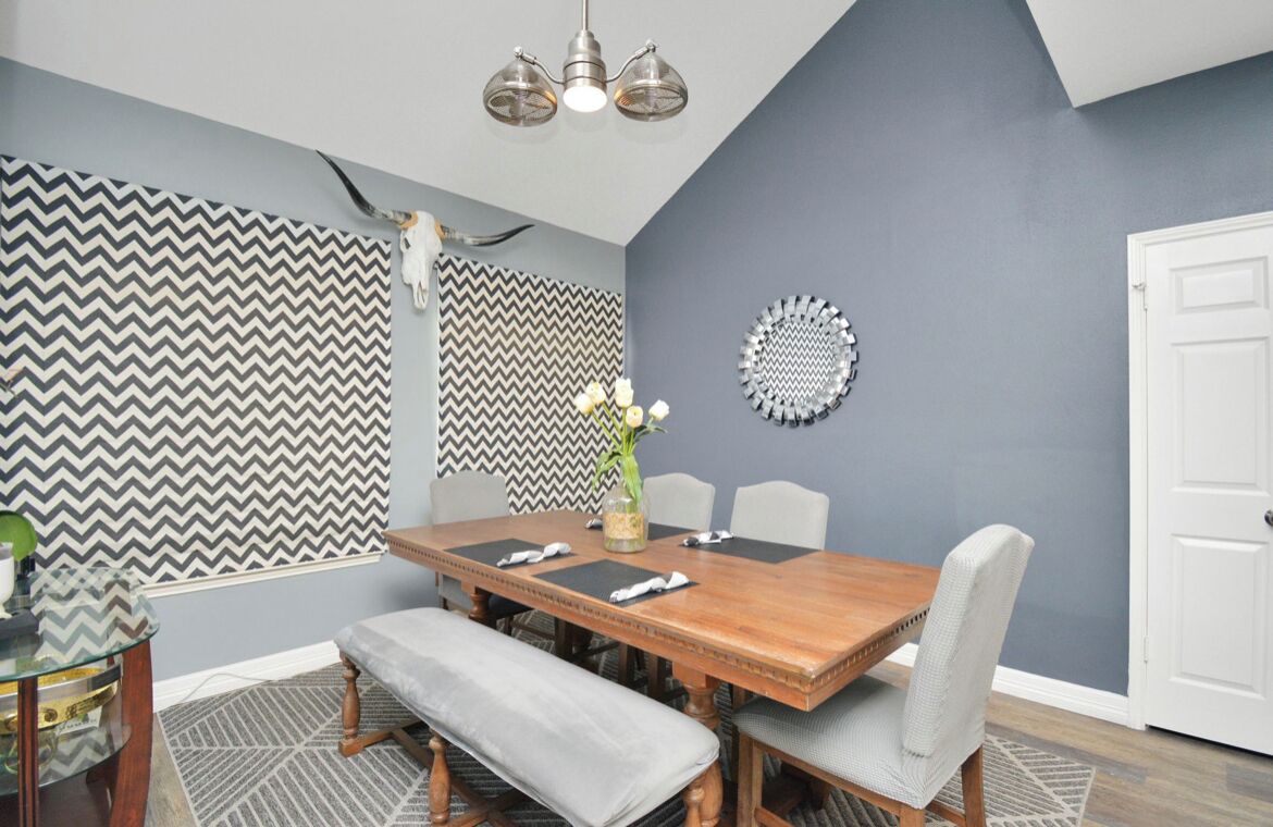 A dining area with a wooden table, grey upholstered chairs, a bench, and a chandelier.