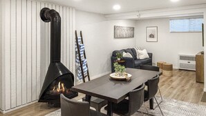 Een gezellige woonkamer met een open haard, een eettafel met stoelen, een bank en een klein bijzettafeltje met een plant.