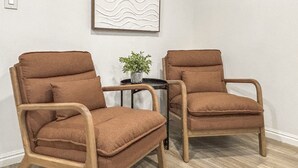 Twee bruine fauteuils met houten frames, een klein rond tafeltje met een bloempot, en een muur met een abstract schilderij met reliëf.