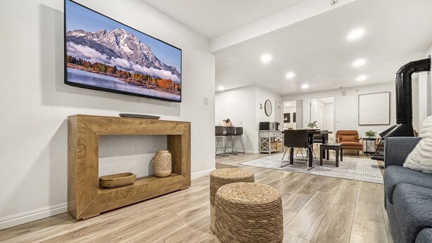 Een moderne woonkamer met een houten tv-meubel, een flatscreen televisie aan de muur en een gezellige zithoek met een bank en poefjes.