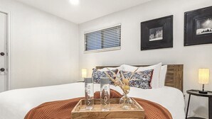 Een netjes ingerichte hotelkamer met een groot bed, een houten dienblad met glazen en een rode gebreide plaid.