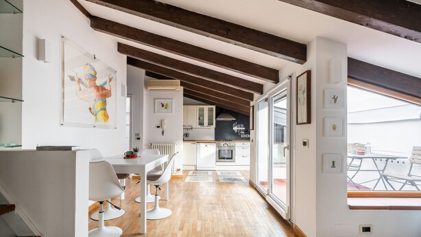 A modern kitchen with wooden flooring, white cabinets, and a large window overlooking a balcony.