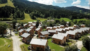 Un gruppo di casette di legno con tetti spioventi, immerse in prati verdi e colline boscose.