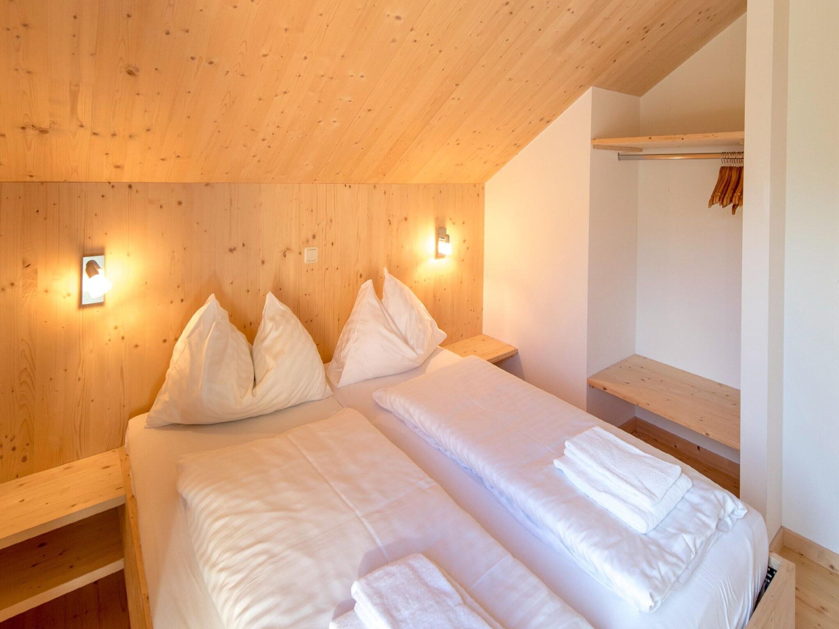 A bedroom with two beds, wooden headboard, bedside lamps, and a wooden shelf.
