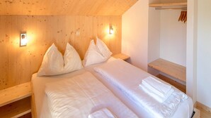 A bedroom with two beds, wooden headboard, bedside lamps, and a wooden shelf.