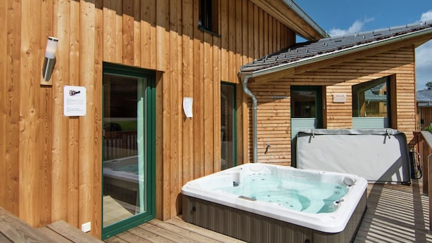 Una cabaña de madera con jacuzzi y terraza cubierta.