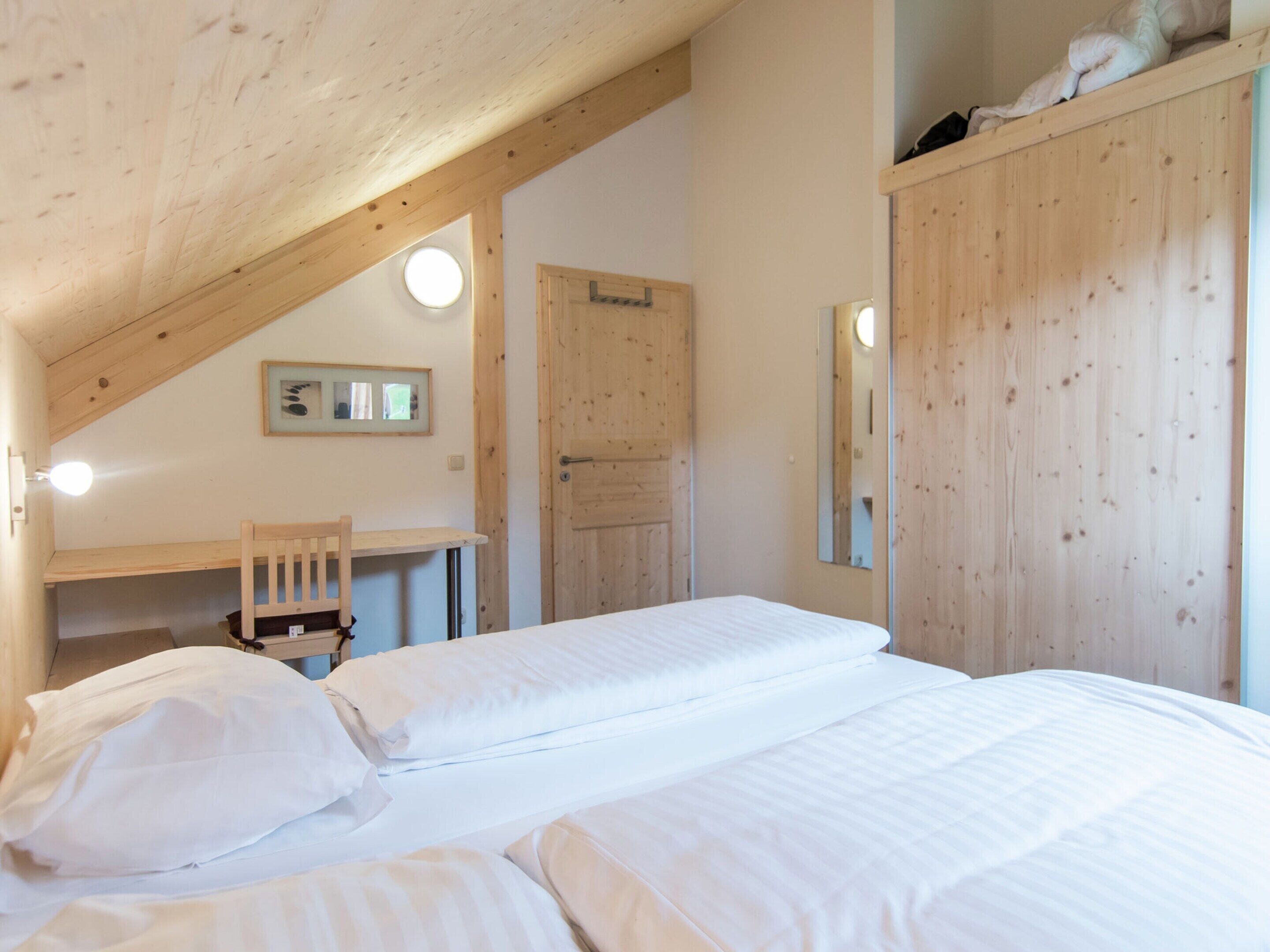 Ein Schlafzimmer mit Holzbalkendecke, einem Schreibtisch, einem Stuhl und einem Bett mit weißer Bettwäsche.