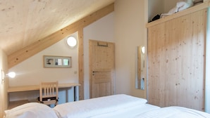 Un dormitorio con techo de madera, un escritorio, una silla y una cama con ropa de cama blanca.