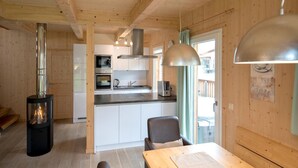 Una cocina acogedora de estilo cabaña, con estufa de leña, armarios blancos y un comedor con mesa y sillas.