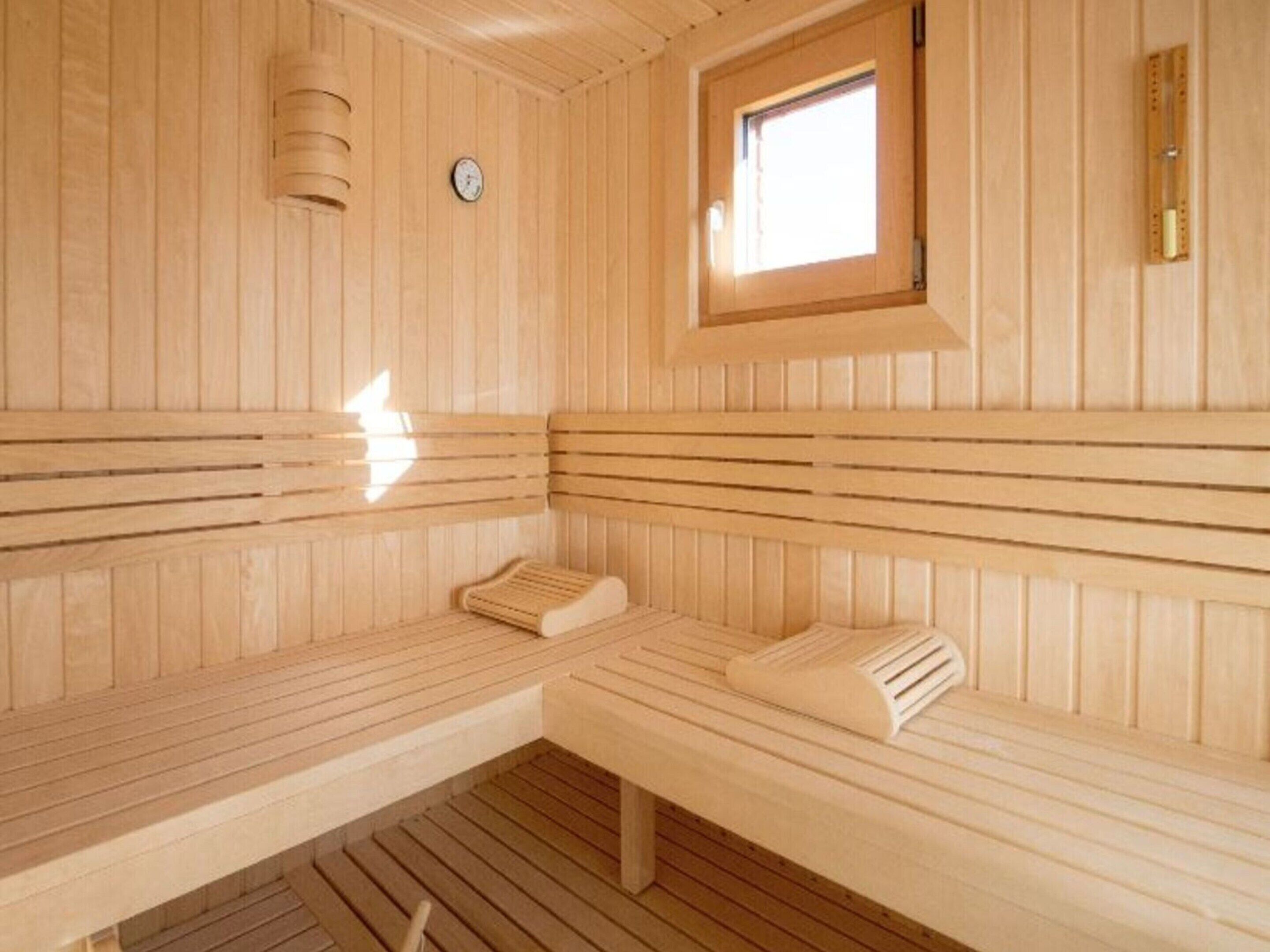 Eine Holzsauna mit Bänken, einem Fenster und einer Wanduhr.