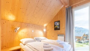 A wooden room with a bed, a wall-mounted lamp, and a window with a view of houses. - Superior Chalet With Sauna (Sankt Georgen am Kreischberg)
