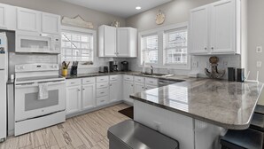 A modern kitchen with white cabinetry, a granite countertop, and a built-in oven. - Aqua Vista #174 - Private Hot Tub, Community Pool, Dog Friendly! (North Topsail Beach)